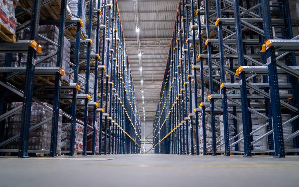 Horizontal camera move between the rows shelves with cardboard boxes and plastic packs on a palette. Logistics center interior full of racks with with large number packs.